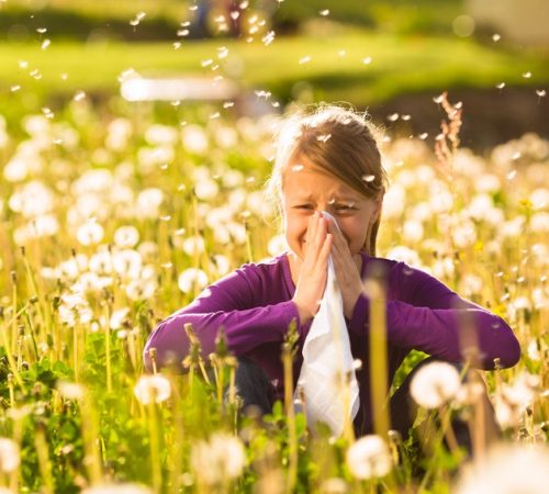 Girl sitting in a meadow with dandelions and has hay fever or allergy